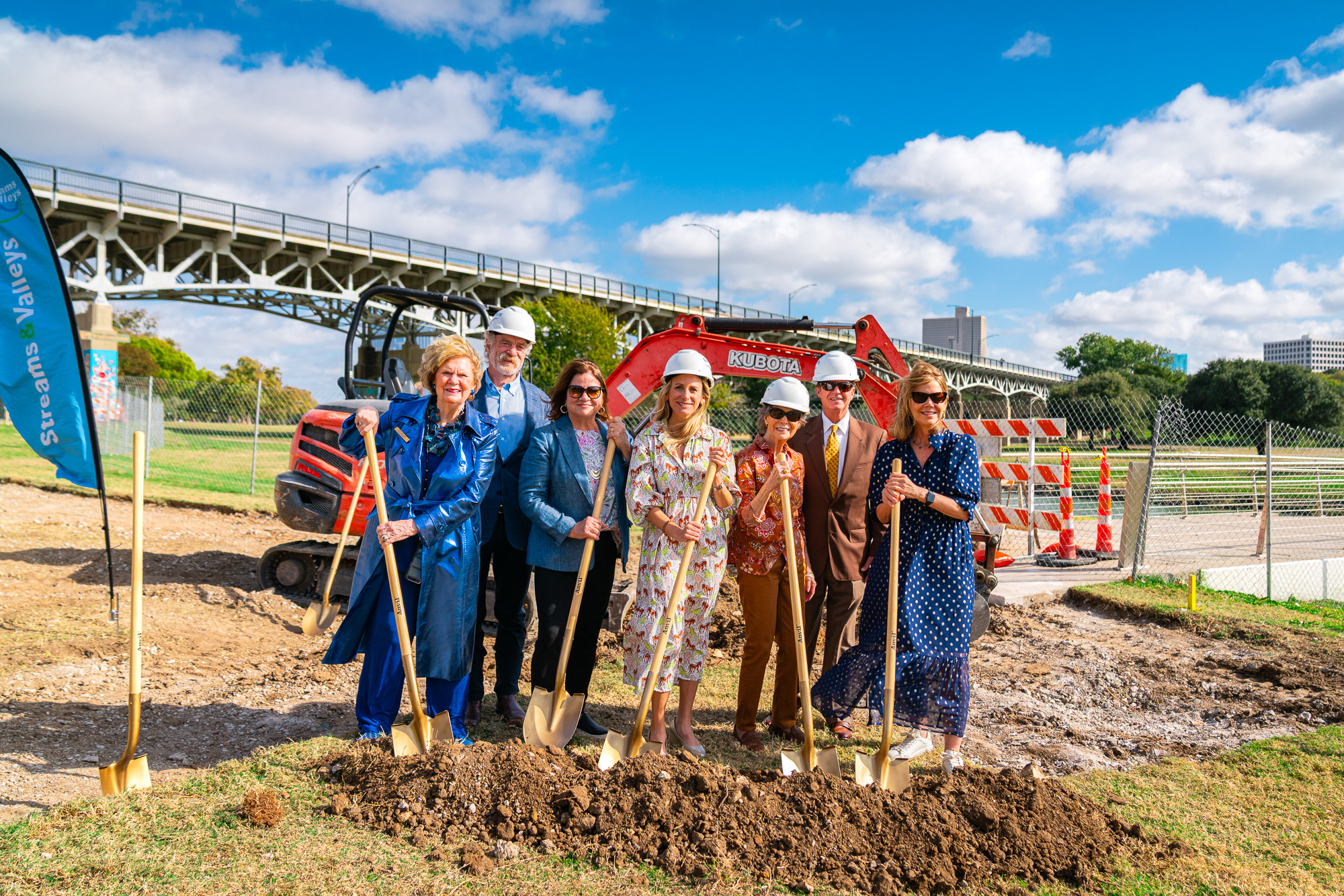 Project partners with gold shovels at the groundbreaking, excavator and bridge behind