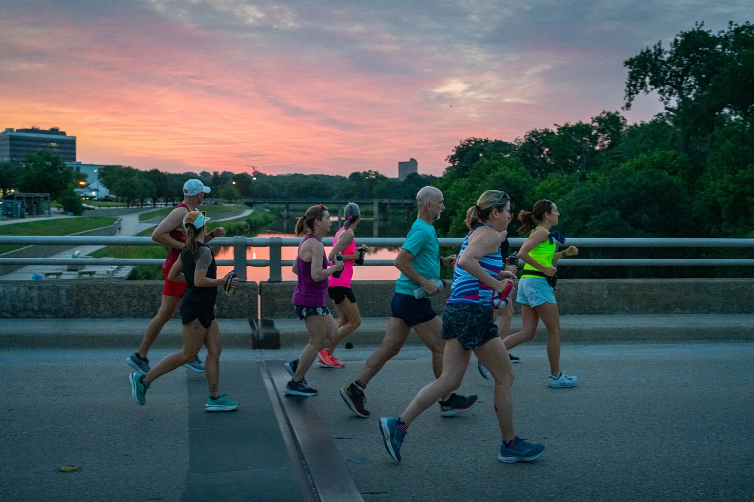 Runners crossing a bridge beneath a colorful sunset